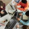 Top view at diverse group of teen school children using computers in classroom studying together at table